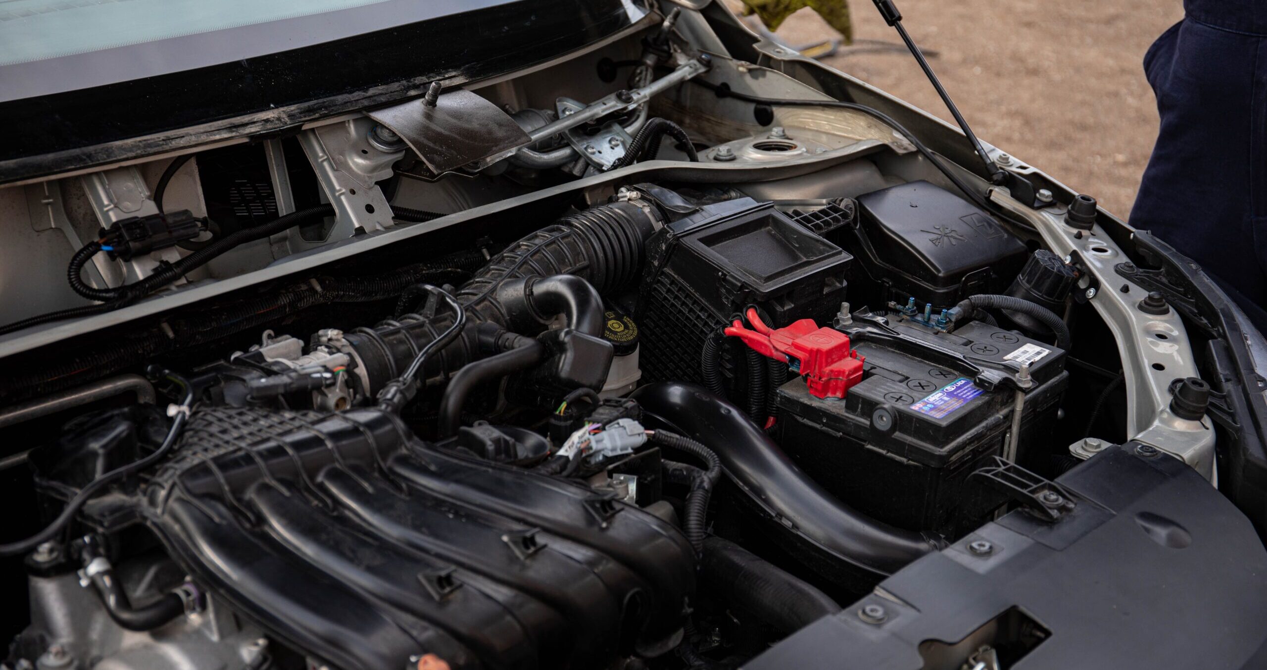 Mechanic inspecting car engine bay and battery during routine maintenance.